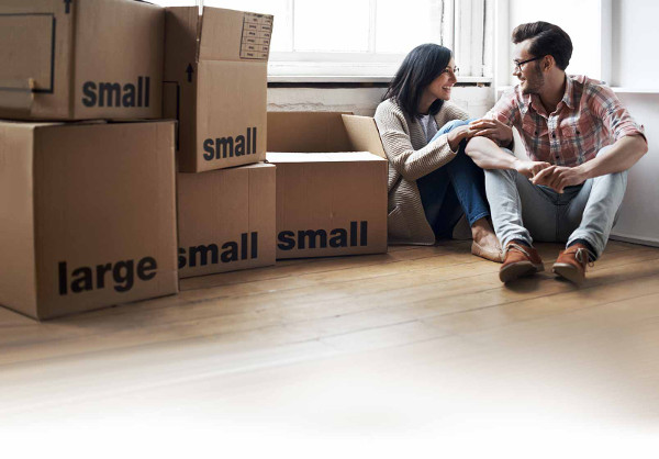 Happy couple sitting on the floor next to five small moving boxes