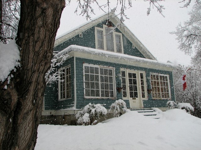 Blue sided house with white trim during a snowstorm