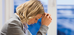 Nicely dressed young woman sitting sadly with her head leaning against her folded hands.