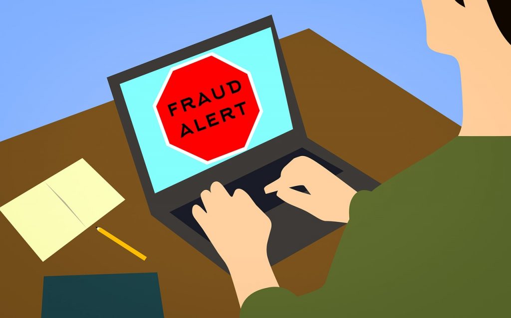 Cartoon image of mail sitting in front of computer screen at a desk with a Fraud Alert in black and red lettering.