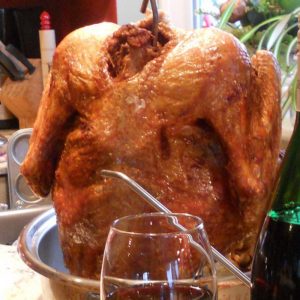 Deep fried turkey standing up in pan draining on a counter next to a sink and a glass of wine