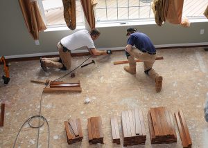 Two contractors in a new house installing new wooden flooring.