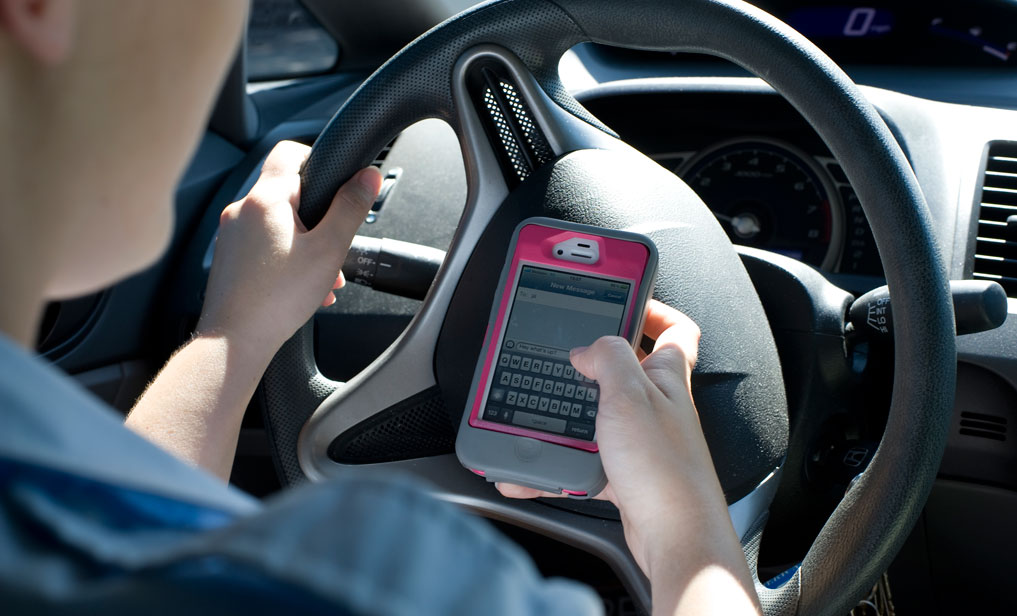 Person sitting behind the wheel of a vehicle texting on a cell phone while driving.