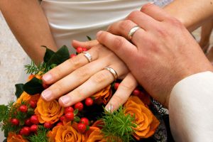 Bouquet of flowers with newly married couples hands on top.