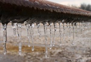 Rusty metal pipe with ice cicles forming on the bottom