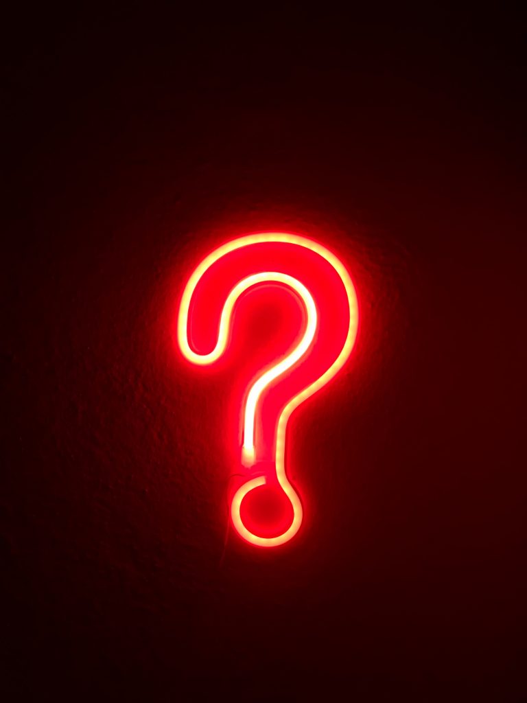 Bright red neon question mark lit up on a dark background