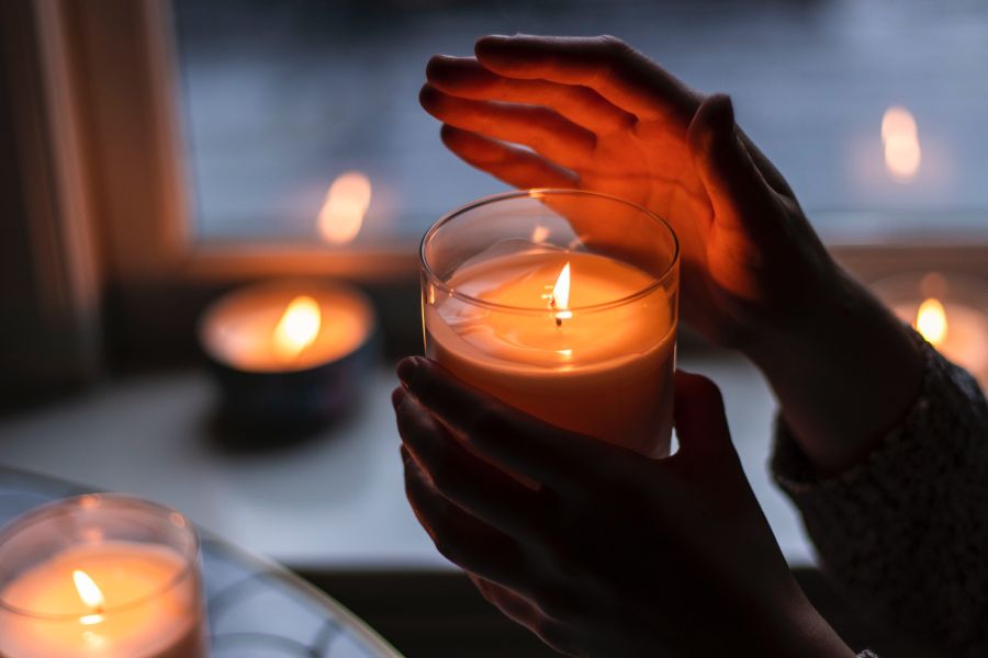Three candles near a window in a dark room one candle being held by hands to protect flame from going out